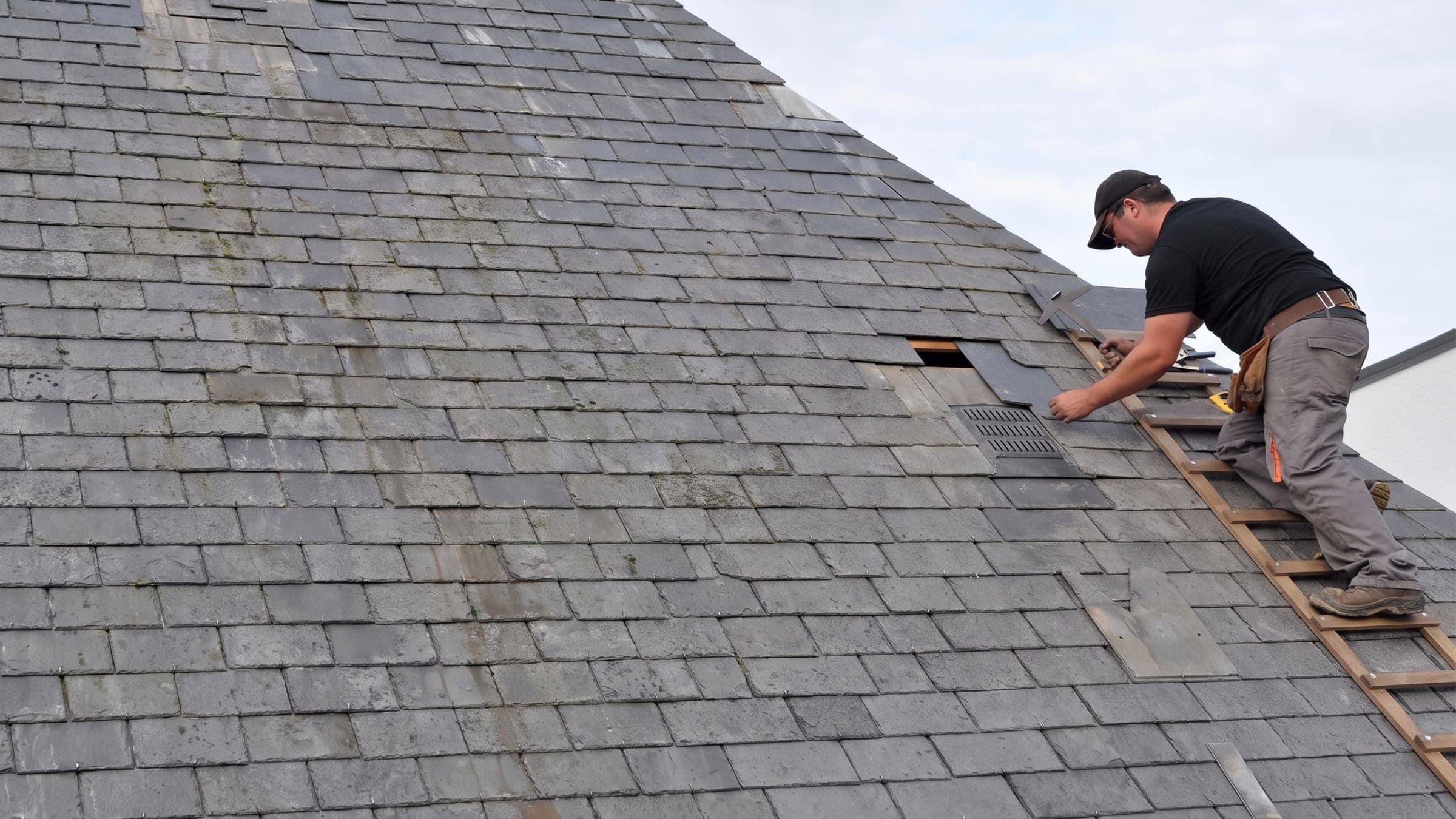 Roofing contractor removing damaged slate shingles during a residential roof repair